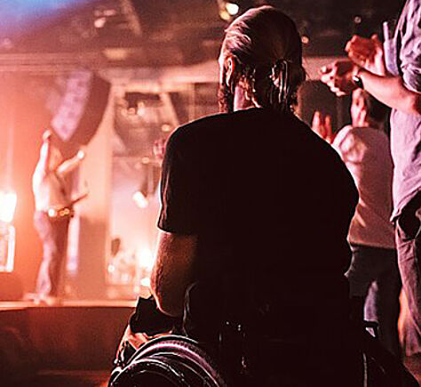 Ein Mann im Rollstuhl, von hinten zu sehen, schaut auf die Bühne mit Musikern
