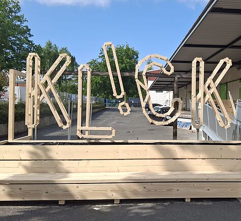 Vor dem Museum steht eine große Holzbank. Darüber bilden große Buchstaben aus hellem Holz das Wort ‚KL!CK‘. Eine Rampe aus Metall führt rechts daneben zum Eingang.