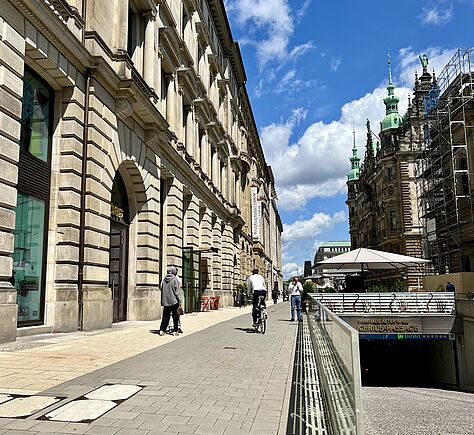 Zu sehen, ist mit malerisch blauem Himmel und weißen Wolken, links das Gebäude des Kunstforums und rechts ist ein Teil des Hamburger Rathauses zu sehen