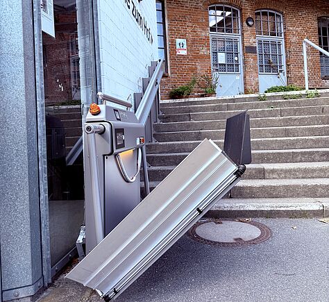 Eingang über eine Treppe zur "Bühne zum Hof". Unten an der Treppe seitlich ein halb aufgeklappter Treppenlifte mit einer Plattform.