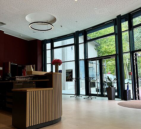 Blick auf den abgesenkten Teil des Empfangstresens auf der linken Bildseite. Rechts ist der eingangsbereich mit bodentiefer Fensterfront zu sehen.