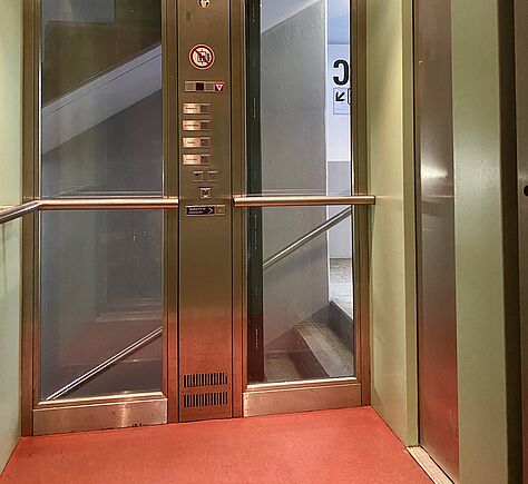 Blick in die Fahrstuhlkabine mit Bedientableau. Glasrückwand.
