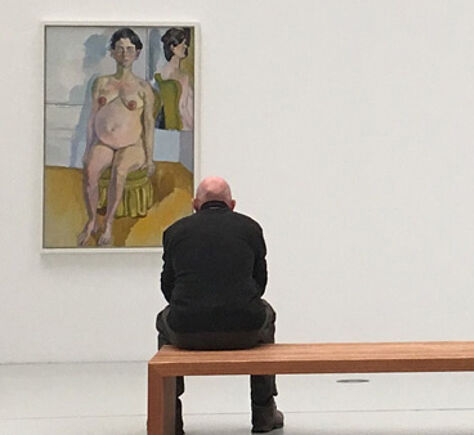 Ein Mann mit Glatze sitzt auf einer Bank und schaut auf das Gemälde einer (nackten) Frau. Er ist von hinten zu sehen, links von ihm das Gemälde.