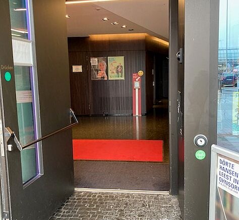 Ebenerdiger Eingang, schwellenlos, drinnen ist ein quer liegender roter Teppich zu erkennen.