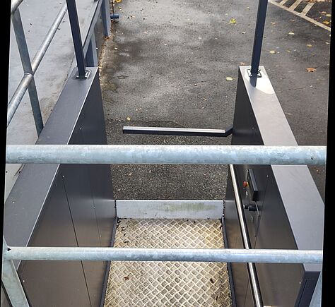 Blick auf die Plattform des Hublifters von der Hinterewand aus gesehen. An der rechten Seitenwand die Bedienelemente. Im Vordergrund 2 Querstangen eines Geländers.