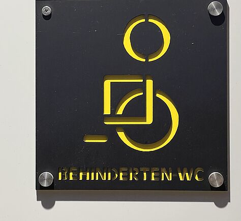 Ein Rollstuhlsymbol in gelb auf einem schwarzen Schild