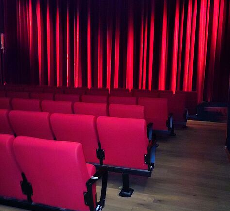 Rote, fest installierte Sesselreihen, vor der Leinwand ein leuchtend roter Vorhang mit vielen Falten