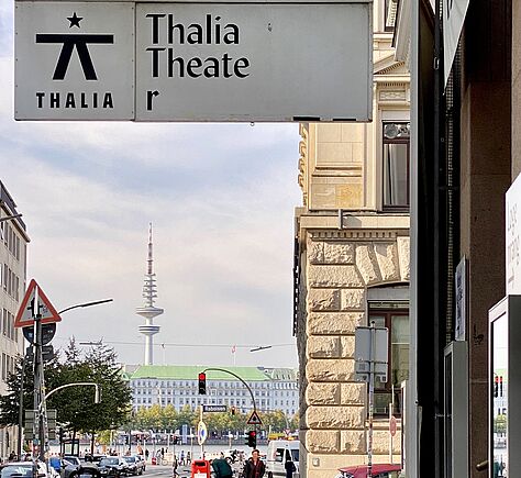 Seitlicher Blick auf das Vordach mit der Beschriftung Thalia Theater. Im Hintergrund Straße, Alster und Fernsehturm.