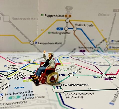 Ein HVV-Stadtplan mit den U-Bahnlinien füllt das Foto aus. In der Mitte eine Rollstuhlfahrern-Mini-Figur.